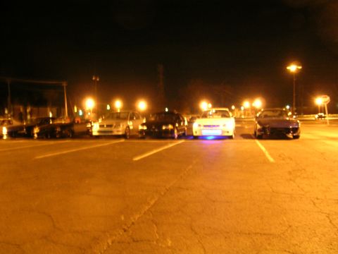 1994 Ford Probe - A group of cars are parked in a lot at night, with one vehicle illuminated by blue underglow lighting.