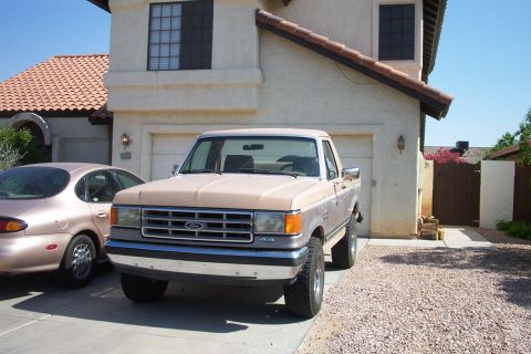 1988 Ford Bronco - This Ford F-150 pickup truck is parked in front of a house with another car beside it.