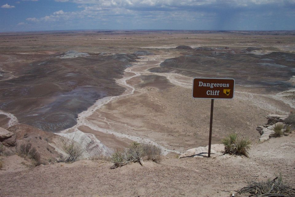 'Dangerous Cliff' warning sign overlooking an eroded desert badlands valley