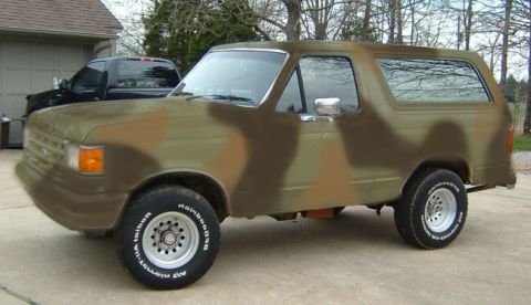 1987 Ford Bronco - This Ford Bronco is painted in a camouflage pattern and is parked in front of a garage.