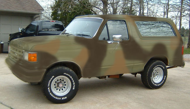 Two-door SUV in green-brown camouflage paint, side view in a driveway