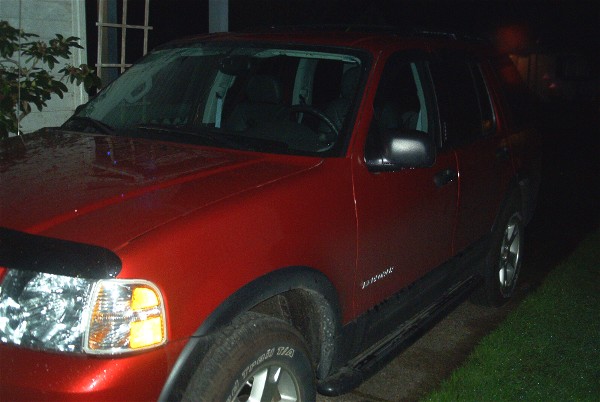 Dark red four-door SUV parked at night, front-left three-quarter view