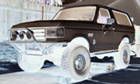1990 Ford Bronco - grainy image of a dark-colored vintage SUV with dual round headlights raised on light-colored stacked supports.