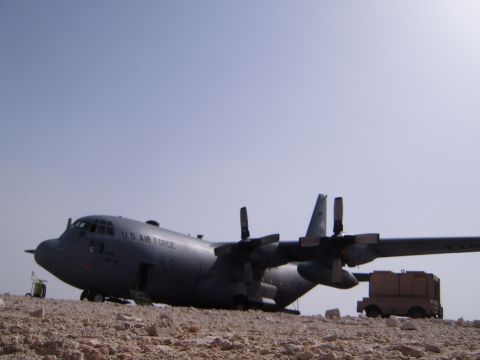 1988 Ford Bronco - A C-130 Hercules aircraft sits on a desert terrain under a clear blue sky.