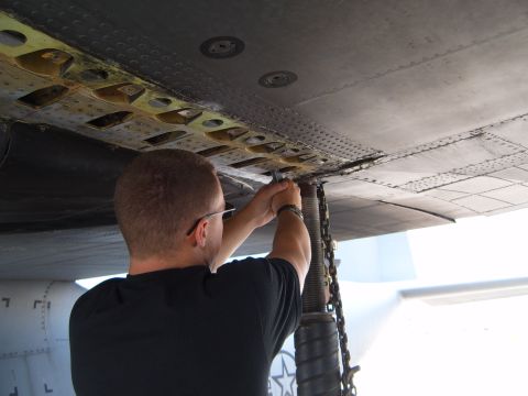 1988 Ford Bronco - A mechanic works on the underside of an aircraft wing, with a chain hoist attached.