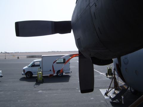 1988 Ford Bronco - A white cargo van is parked on an airport tarmac next to the engine of a large aircraft.