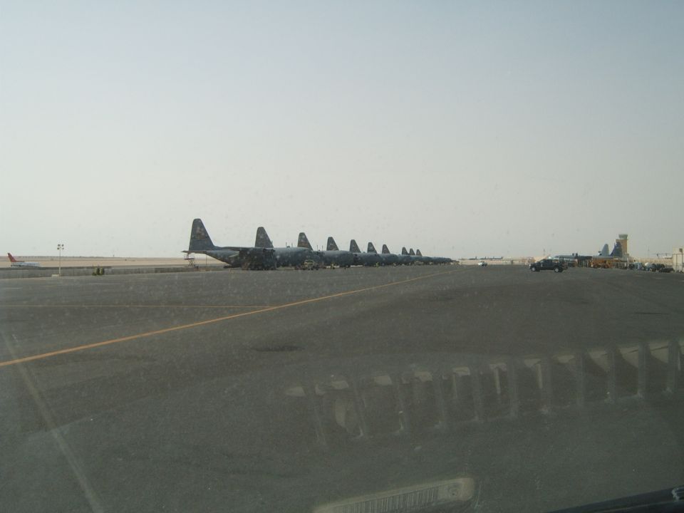 Row of parked military cargo planes on an airfield with a few vehicles in the distance