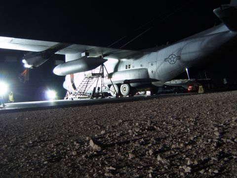 1988 Ford Bronco - A large military cargo plane is parked on a tarmac at night, illuminated by ground lights.