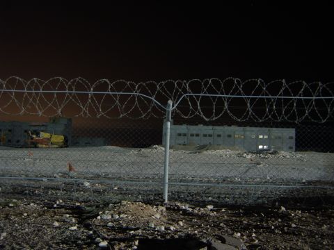 1988 Ford Bronco - Nighttime view of industrial buildings behind a barbed wire fence.