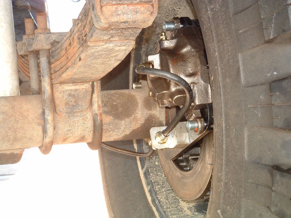 Rear disc brake caliper and rotor with new brake hose on rusty leaf-sprung axle, tire beside it
