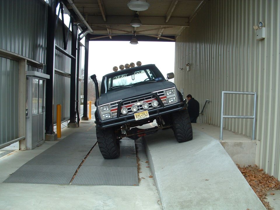 Flat-black lifted squarebody Chevy pickup, front view, roof lights, mud tires
