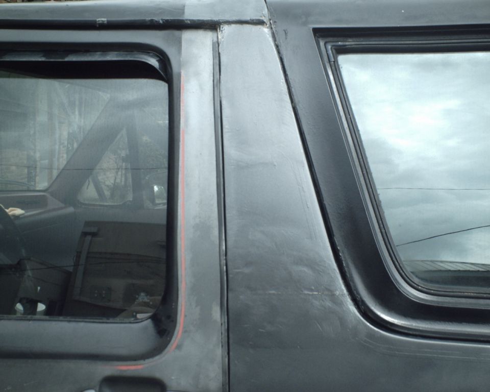 Side view of a dark SUV's rear door and window with a red stripe detail