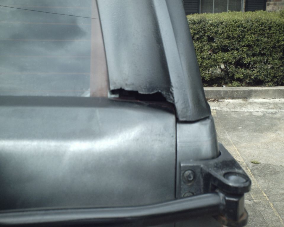Close-up of damaged rear window frame on a vehicle. Supermotors.net logo visible