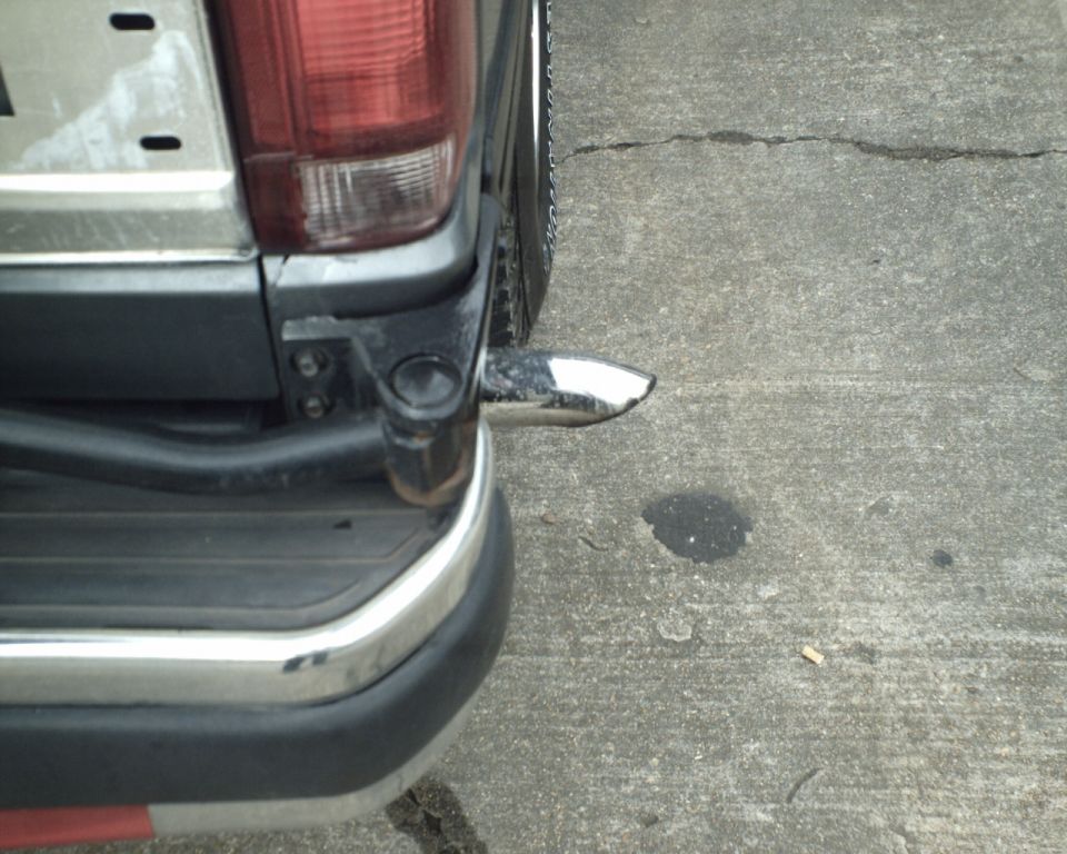 Damaged chrome rear bumper corner bent away from gray and red vehicle body on concrete