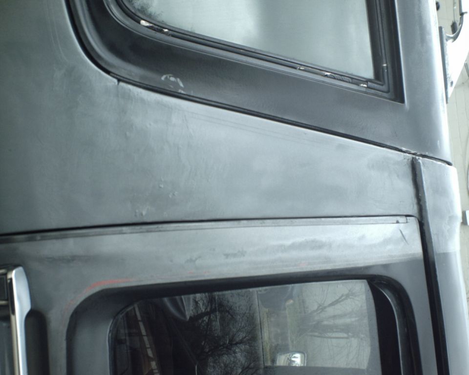 Close-up of a dark gray vehicle body panel with window trim and a SuperMotors watermark