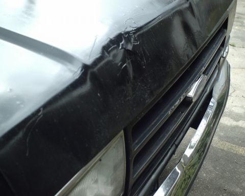 1987 Ford Bronco - Close-up of the front grille and damaged hood of a black vehicle.