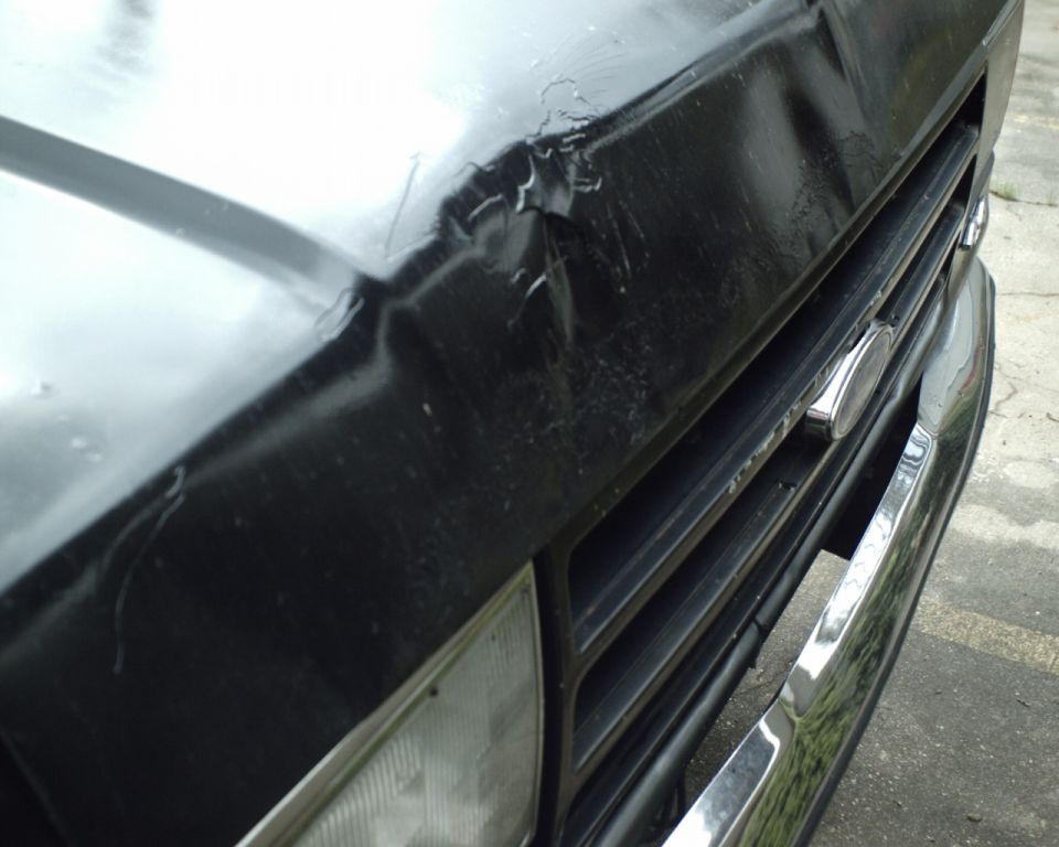 Front grille and dented hood of a black 1987 Ford Bronco