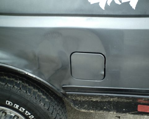 1987 Ford Bronco - The rear quarter panel of a vehicle shows a dent and a fuel door.