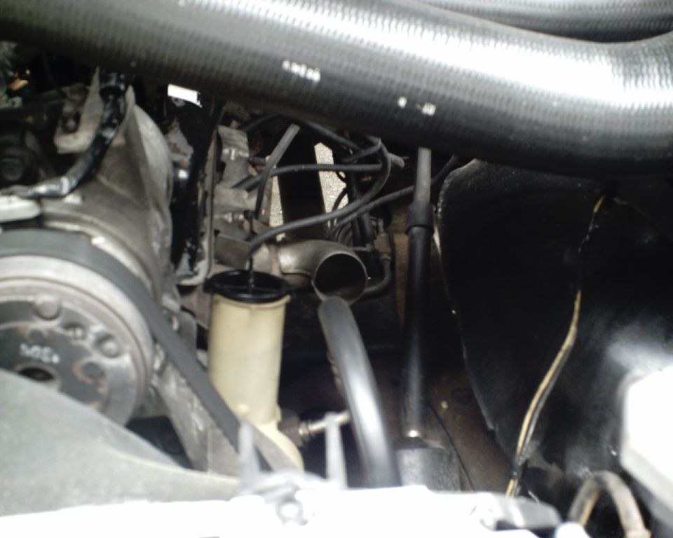 Engine bay close-up showing power steering reservoir, pulley, belt, and black hoses