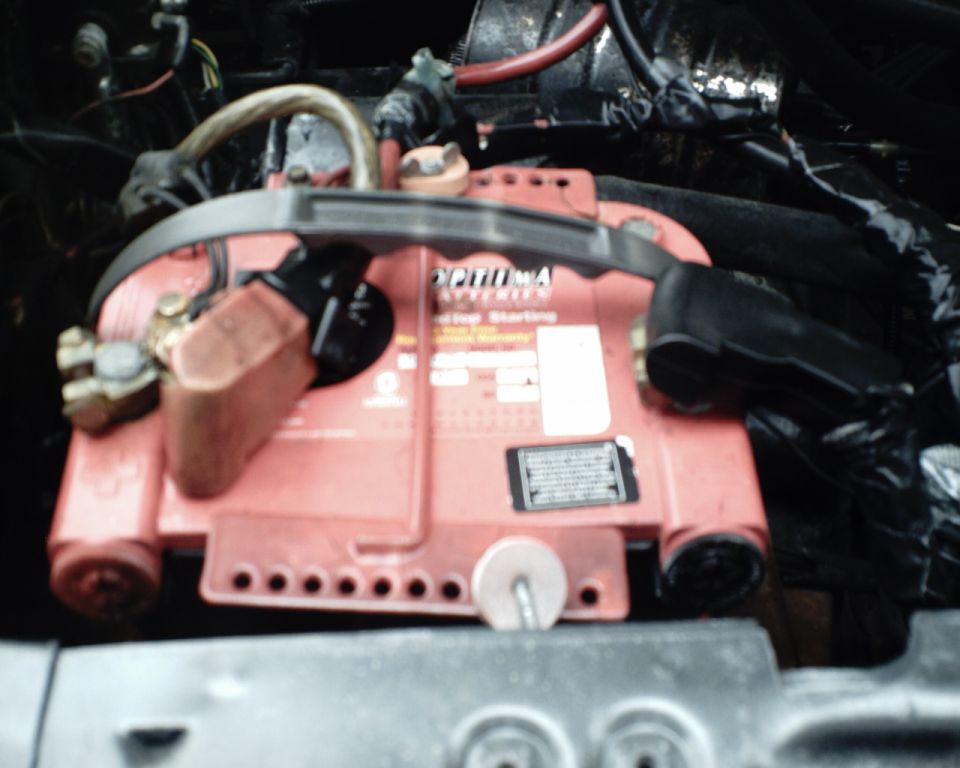 Red Optima car battery with black terminals and cables, top view