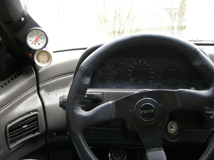 Car interior with a black steering wheel and two gauges visible on the left