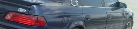 1993 Ford Taurus - The rear of a dark blue Ford Taurus sedan is visible, a spoiler and a Ford emblem.