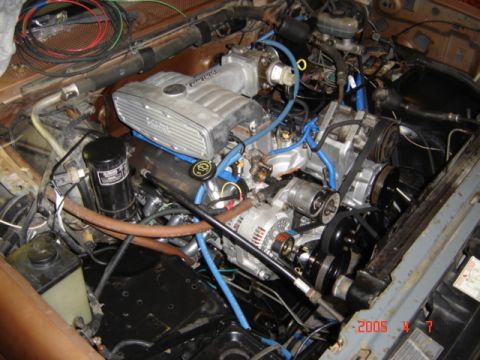 1990 Ford Bronco - Engine bay of a truck with a fuel-injected V8 nearly buttoned up, showing a polished aluminum upper intake plenum, blue plug wires and vacu…