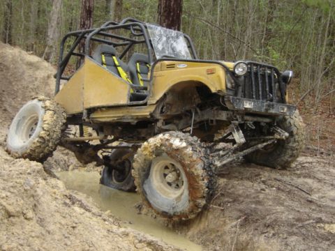 1989 Ford Bronco - This heavily modified off-road buggy tackles a challenging muddy obstacle with its large tires and reinforced frame.