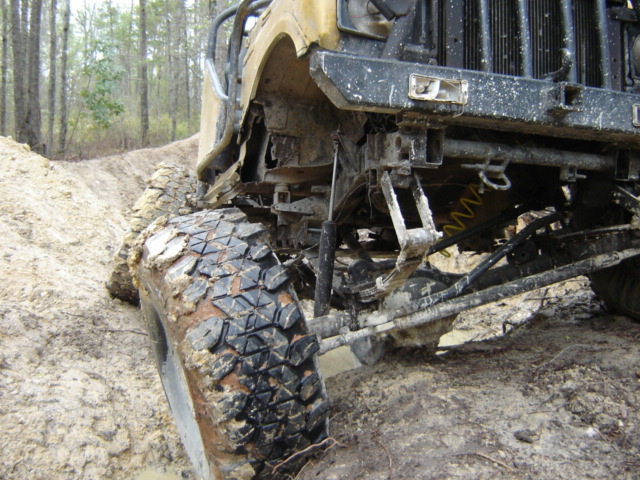 Off-road vehicle's front suspension and large tire covered in mud on a dirt track