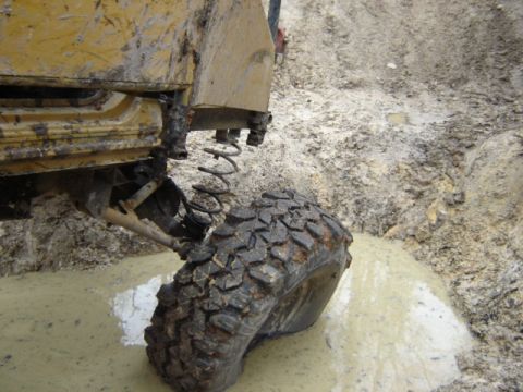 1989 Ford Bronco - A yellow off-road vehicle navigates a muddy terrain, with its tire deep in the muck.