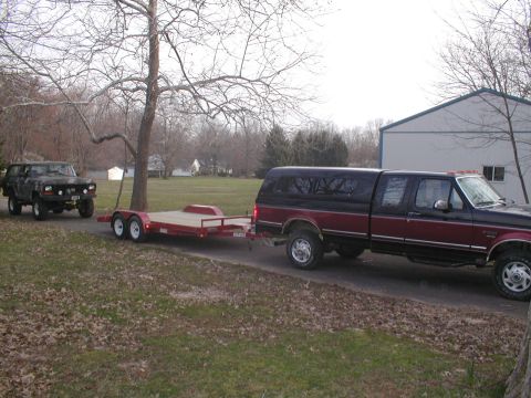 1979 Ford Bronco - A dark green 1978 Ford Bronco is being towed on a red trailer by a two-tone pickup truck.