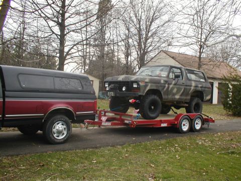 1979 Ford Bronco - A camouflaged Ford Bronco is loaded onto a trailer, towed by a pickup truck.
