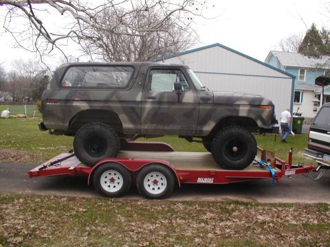 1979 Ford Bronco - A camouflaged Ford Bronco is loaded onto a red trailer, ready for transport.
