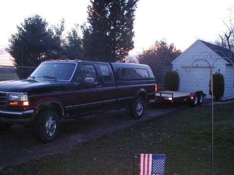 1979 Ford Bronco - A Ford F-Series truck is hitched to a trailer in front of a residential garage.