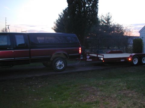 1979 Ford Bronco - A red and black pickup truck is seen from the side, towing a flatbed trailer.