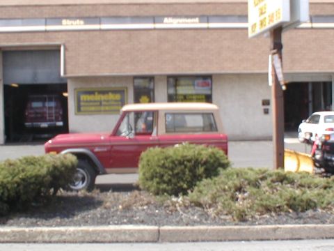 1979 Ford Bronco - 1979 Ford Bronco with tan top parked outside a Meineke auto shop.