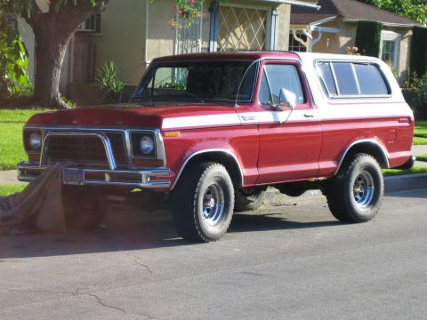 1990 Ford Bronco - red-and-white late-1970s Ford Bronco with a chrome grille, FORD lettering on the hood and a removable hardtop sits on a suburban street.