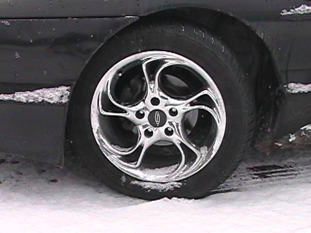 Chrome five-spoke aftermarket wheel on a black car in snow