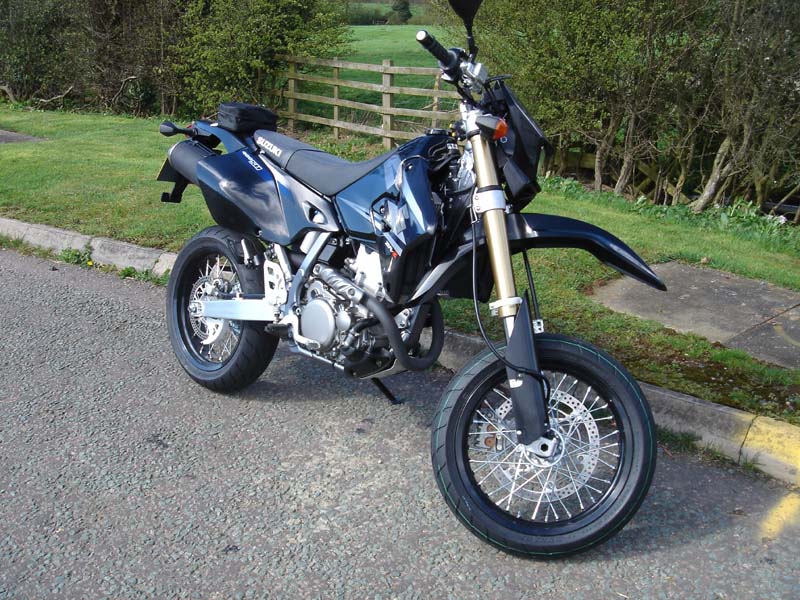 Blue Suzuki supermoto motorcycle on side stand with spoked wheels and gold forks