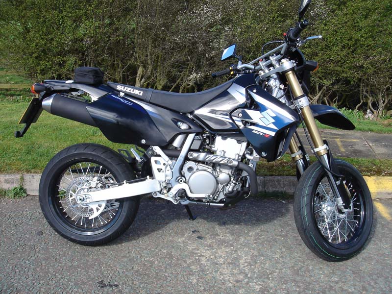 Dark blue Suzuki supermoto motorcycle parked on pavement, side view