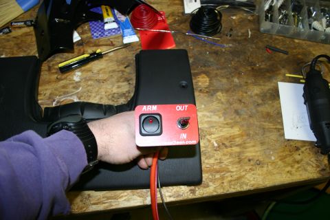 2003 Jeep TJ - A red switch panel with 'ARM OUT' and 'IN' labels is held by a hand, showing a toggle switch and a push button.