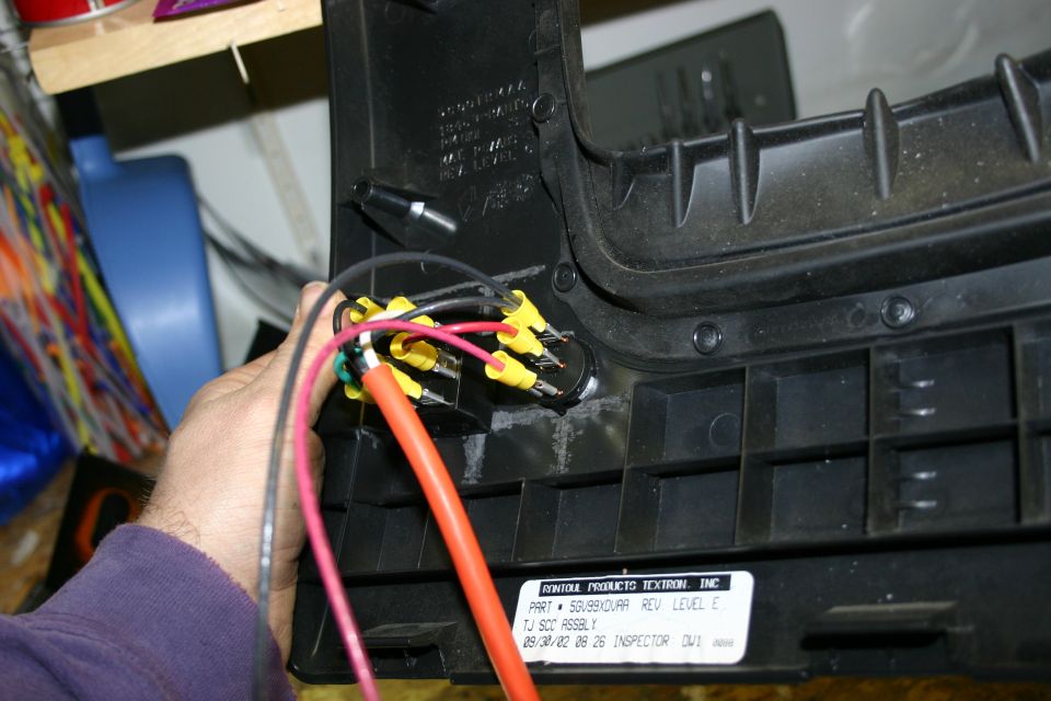 Hand connecting wires to a switch on a black plastic part labeled 'TJ SCC ASSEMBLY'