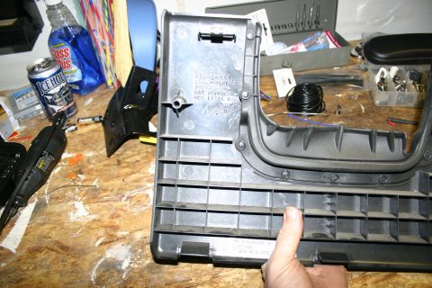 2003 Jeep TJ - A person's hand holds a plastic automotive interior part on a cluttered workbench with tools and supplies.