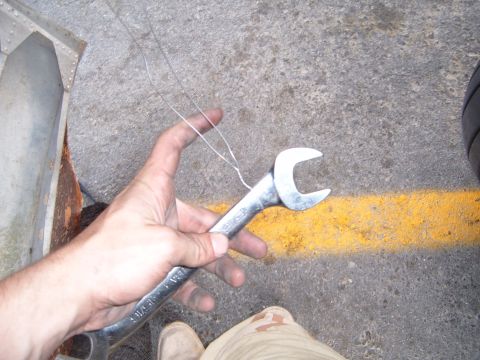 1988 Ford Bronco - A hand holds a wrench and wire against a paved surface with a yellow line.