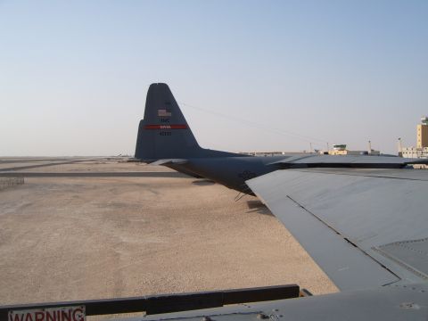 1988 Ford Bronco - A C-130 Hercules aircraft sits on the tarmac under a clear sky, with a control tower visible in the distance.