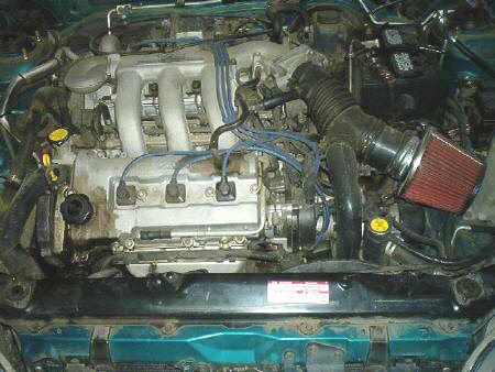 1994 Mazda MX-3 - Engine bay of a 1994 Mazda MX-3, showing the V6 engine with modifications and coolant reservoir.