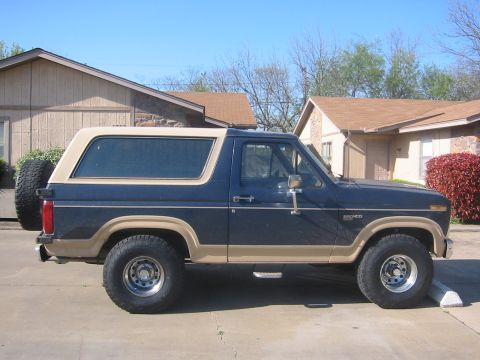 1986 Ford Bronco - A blue 1986 Ford Bronco is parked in front of a residential building.