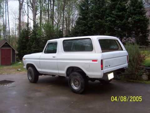 1979 Ford Bronco - A white 1978 Ford Bronco is parked outside on a paved surface with trees and a small shed visible.