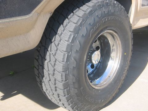 1986 Ford Bronco - A close-up view of a Nitto Terra Grappler tire mounted on a chrome wheel, with a portion of the vehicle's body visible.