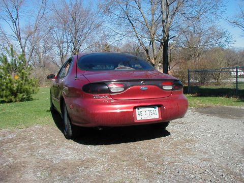 1997 Ford Taurus - The rear of a red Ford Taurus is parked on a gravel driveway under a clear sky.